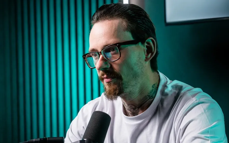 Ben Hawksworth in a studio, glasses on, sitting at a microphone